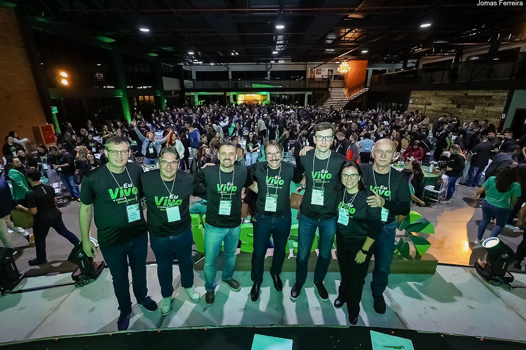 Equipe da Capital Relacional no palco de um evento, com a plateia ao fundo